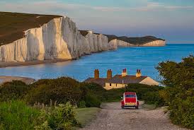 The cliffs are named the seven sisters cliffs because of the seven hilltops that make up the silhouette of the cliffs. A Beautiful Sunset At Seven Sisters Cliffs In England With A Red Car Passing By Photograph By George Afostovremea