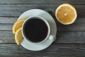 a glass of black coffee next to a whole lemon and a sliced lemon, illustrating if coffee and lemon juice help you lose weight