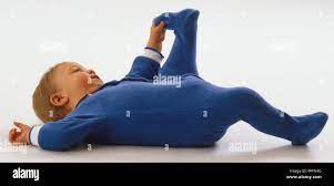 Baby Wearing Blue Jumpsuit Lying On Her Back Grabbing One Foot With Her Hand Showing Flexibility Stock Photo Alamy