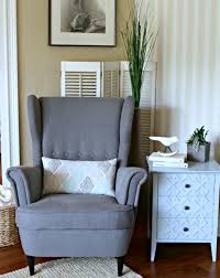 Modern living room features a gilded leaf chandelier illuminating an armless sapphire blue velvet sectional on a light gray wall, oval wooden table atop a gray and blue rug, and a corner accent table boasting a brass lamp with yellow shade. Target In Zee Home