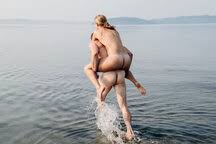 Nackter Mann gibt nackte Frau huckepack ins Wasser, lizenzfreies Stockfoto