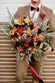 Maybe you would like to learn more about one of these? Vintage Bohemian Inspired Florida Wedding Bouquet Textured Flowers With Orange Purple Yellow Red Eggplant And Ivory Floral Stems Thistle Roses Groom Wearing Neutral Tone Brown Boho Suit With Velvet Bow Tie