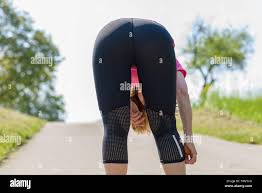 Athletic fit woman in sportswear bending over viewed from the rear on a  country road as she pauses for a moment while out jogging Stock Photo -  Alamy