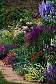 Beautiful Mix Of Perennial Flowers Bloom In A Wide Range Of Blue White Yellow Red And Purple Colors Against A Brown Stone Wall Plants Cottage Garden Perennials