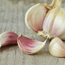 Clove of garlic on a cutting board with a knife and an old tea towel. 5 Swaps For Fresh Garlic Cloves