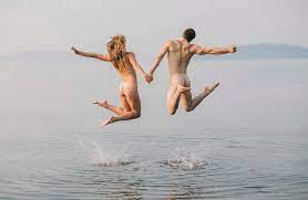Rear view of nude couple in water jumping in mid air stock photo