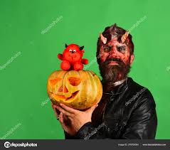 man wearing scary makeup holds pumpkin