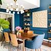 Chic contemporary dining room features a suzanne kasler morris lantern hung from a peacock blue vaulted ceiling between skylights and over a black and gold dining table surrounded by gold and black velvet dining chairs and a vintage wood. 1