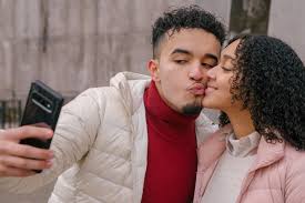 ethnic couple kissing and taking selfie