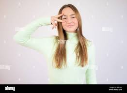 Attractive young girl, showing two fingers forming the letter V like  victory, covering her eye with piece gesture Stock Photo - Alamy