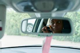 woman putting on makeup in a car mirror