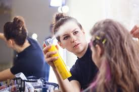 artist applying hairspray on model s hair