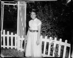 Portrait Of Woman Wearing Horizontally Striped Dress With Light Colored Collar And Cuffs Dark Belt And Eyeglasses Posed In Front Of Picket Fence And Trellis Cmoa Collection