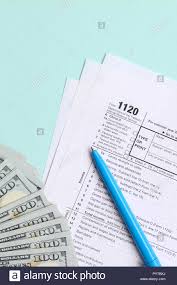 1120 Tax Form Lies Near Hundred Dollar Bills And Blue Pen On