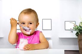 baby eating yogurt with a spoon