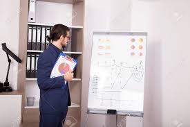 Businessman With A Folder With Charts In Hands Next To A Flip Chart
