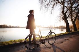 Eyes glint under golden skies. Teenager Boy Standing With Bicycle By River At Sunset Trees Sunlight Stock Photo 193437628