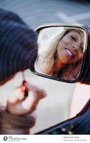 ethnic female applying makeup near car