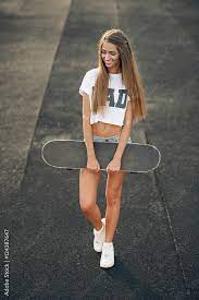 Beautiful young and sexy smiling teen girl in a white T-shirt and shorts  standing with skateboard in hands Stock Photo | Adobe Stock