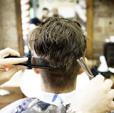 Close up of barber in latex gloves holding hair comb and scissors while cutting hair of man. Is An Expensive Haircut Worth It How Much Men Should Pay