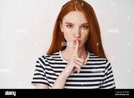Close-up of young ginger girl with serious face showing taboo sign, hushing  at you, telling a secret, white background Stock Photo - Alamy