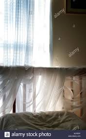 A Simple Bedroom Under Ambient Light From The Window Coming In Through Blue Sheer Curtains To Light Up The Sheer Fabric Wrapped Around The Headboard Of The Bed Stock Photo Alamy