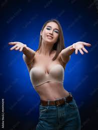 Beautiful mixed race Asian girl with big breasts, wearing a bra and jeans,  smiles and holds out her hands forward. Advertising, commercial design.  Stock Photo | Adobe Stock