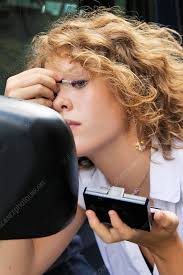 woman applying makeup in car mirror