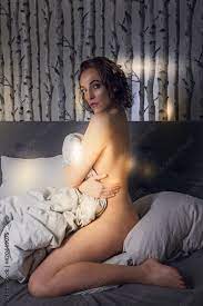 Nackte Frau im Bett sitzend , die Ihrem Körper mit einer Bettdecke  verdeckt, bei Sonnenlicht am morgen. Stock-Foto | Adobe Stock