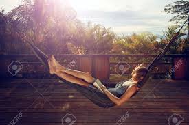 彼女の手で本を持つ女性は、休暇中にジャングルの中で夕日の背景にテラスのハンモックで休んでいます。 の写真素材・画像素材. Image 82307999.