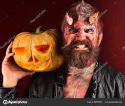 man wearing scary makeup holds pumpkin