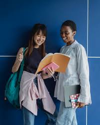 Smiling multiracial girlfriends sharing workbook while doing homework ·  Free Stock Photo