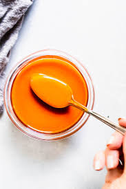 hand holding spoon dipped into jar of buffalo sauce