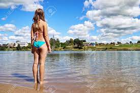 Teenager Girl Wearing Bikini Stands In The Water Of Russian Suburban Lake  And Enjoys Warm Weather And Is Going To Swim At Summer Vacations. Summer  Bathing In A Country Lake Or Pond