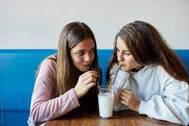 Girlfriends Sharing A Glass Of Milk Or White Drink