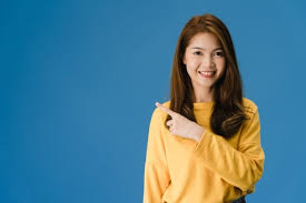 Free Photo | Portrait of young asian lady smiling with cheerful expression,  shows something amazing at blank space in casual clothing and looking at  camera isolated over blue background. facial expression concept.