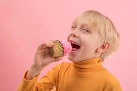 Premium Photo | Fairhaired boy eats cupcake with pink icing grinning child  wants to bite off piece of muffin side view