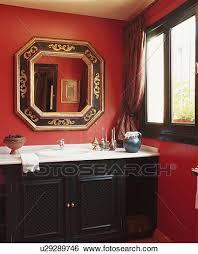 White (light gray?) cabinets support sand beige stone tops that seamlessly fade into gray wall tiles. Hexagonal Gilt Mirror Above Basin Set Into Black Vanity Unit In Red Bathroom Stock Photograph U29289746 Fotosearch