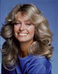 70s hairstyles farrah fawcett long golden blonde 70s flipped out waves wearing a blue top