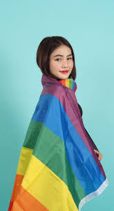 Portrait of young girl holding an LGBT flag standing against a blue green  background studio. Asian LGBTQ woman with rainbow scarf on neck. look smart  bright and energetic cheerful. LGBTQ concept. peace;