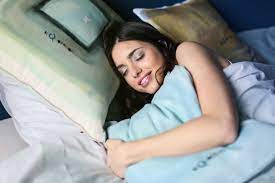 a girl with dark hair sleeping and holding a pillow close to her.