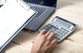 Business Person Calculating Budget With Calculator At Desk Stock