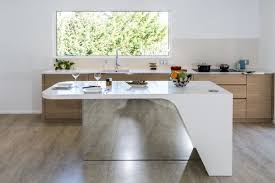 The kitchen island's beige speckled granite countertop is held up by a dark wooden base with pedestals. Stylish Kitchen Layout Centered Around A Mirrored Island