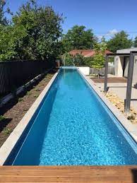 Narrow backyard pool clad with white tiles next to a wooden deck. 13 Lap Pool Dimensions And Cost Ideas Pool Pool Designs Swimming Pool Designs