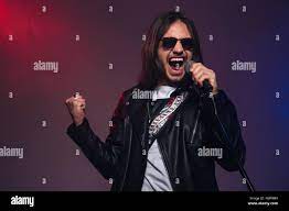 Séduisant jeune chanteur à lunettes avec des cheveux longs avec microphone  de chant sur fond de fumée colorée Photo Stock - Alamy
