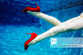 Mature woman wearing red dress and high heels, swimming, underwater view