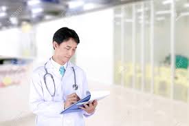 Asian Male Doctor With Stethoscope Writing On A Medical Record