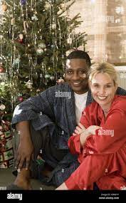 Portrait of a mature interracial couple in pajamas sitting by Christmas  tree Stock Photo 