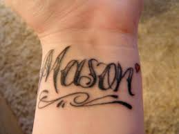 The wrist is a great spot for a heart tattoo with names, especially if you want to show love for your family or honor lost loved ones. Black Ink Mason Lettering With Tiny Red Heart Tattoo On Wrist
