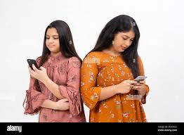 Two young teenager Indian girls busy on their smart phones, standing  against white studio backdrop Stock Photo - Alamy